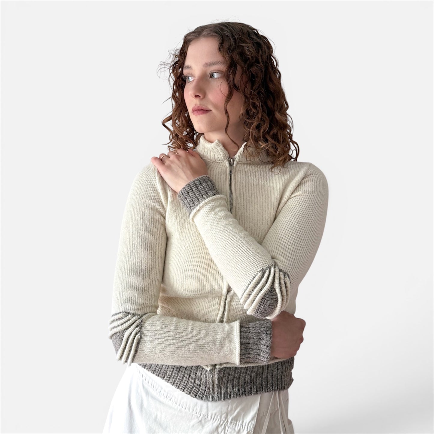 Woman wearing a cream-colored sweater with gray ribbed cuffs and hem on a white background